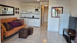 A compact living space with a sofa, ottomans, a television, a kitchen area, and a refrigerator. - Apartment Natura Beach 203 with parking space - 4 people (AGDE)