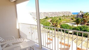 A balcony with white plastic chairs, a view of a hotel complex, and a beach area with palm trees. - Natura Beach - Apartment NB303 - 8 people (AGDE)