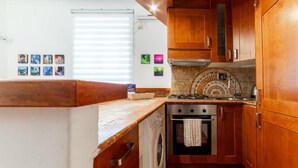 Een kleine keuken met houten kastjes, een inbouwoven, een wasmachine en een betegelde achterwand.