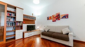 Een woonkamer met een bank, een televisie, een boekenkast en kunstwerken aan de muur.
