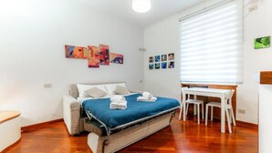 Een slaapkamer met een bed, een bureau en stoelen, een raam met zonwering en kunstwerken aan de muren.