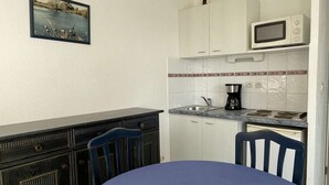 Een kleine keuken met een magnetron, koffiezetapparaat en een spoelbak. Er is een eettafel met stoelen en een schilderij aan de muur.