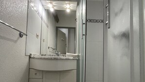 Een badkamer met een wit wastafelmeubel, een spiegel, een douchecabine en een handgreep.