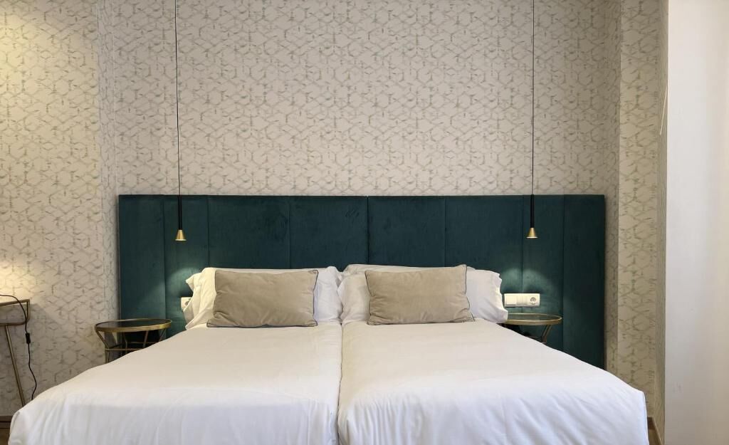 Un lit double avec une tête de lit sombre, deux tables de chevet et un mur orné d’un motif.