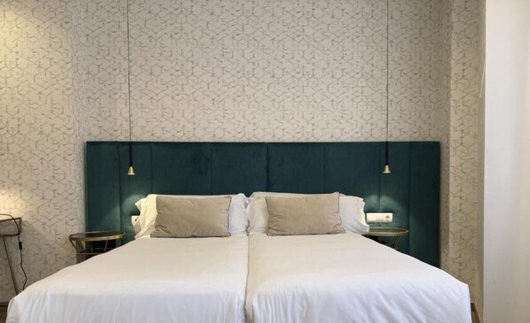 Un lit double avec une tête de lit sombre, deux tables de chevet et un mur orné d’un motif.
