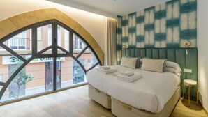 A hotel room with a large arched window, a bed with white linens, and a green upholstered headboard. - Souvirón de Torres (Malaga)
