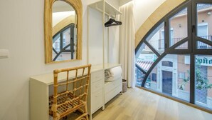 A room with a large window, a white dresser, a wicker chair, and a mirror. - Souvirón de Torres (Malaga)