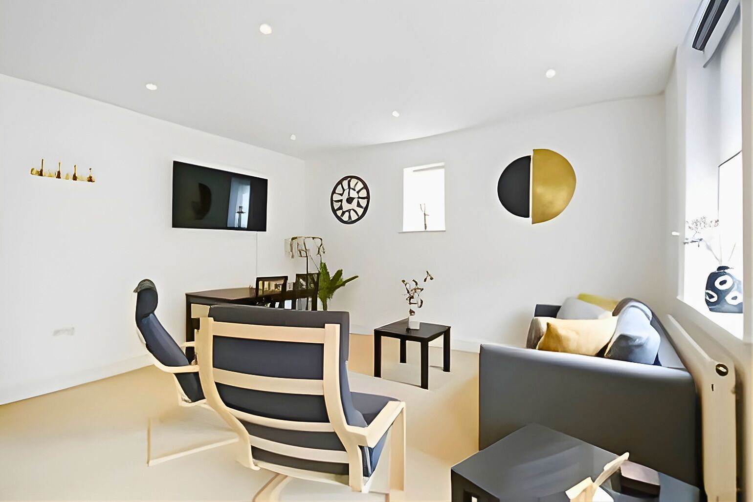 A modern living room with a dining area, a sofa, and a TV mounted on the wall.