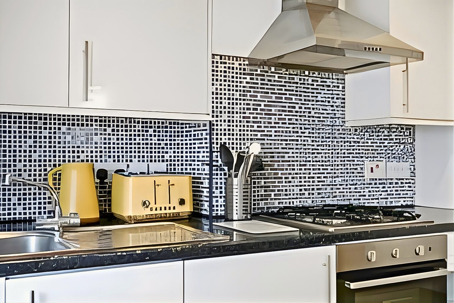 A modern kitchen with white cabinets, a black countertop, a yellow appliance, and a patterned backsplash.