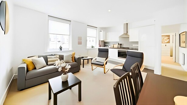 A modern living room with a sofa, chairs, a coffee table, and a kitchen in the background. - Charming 1-Bed Apartment in Lewisham (London)