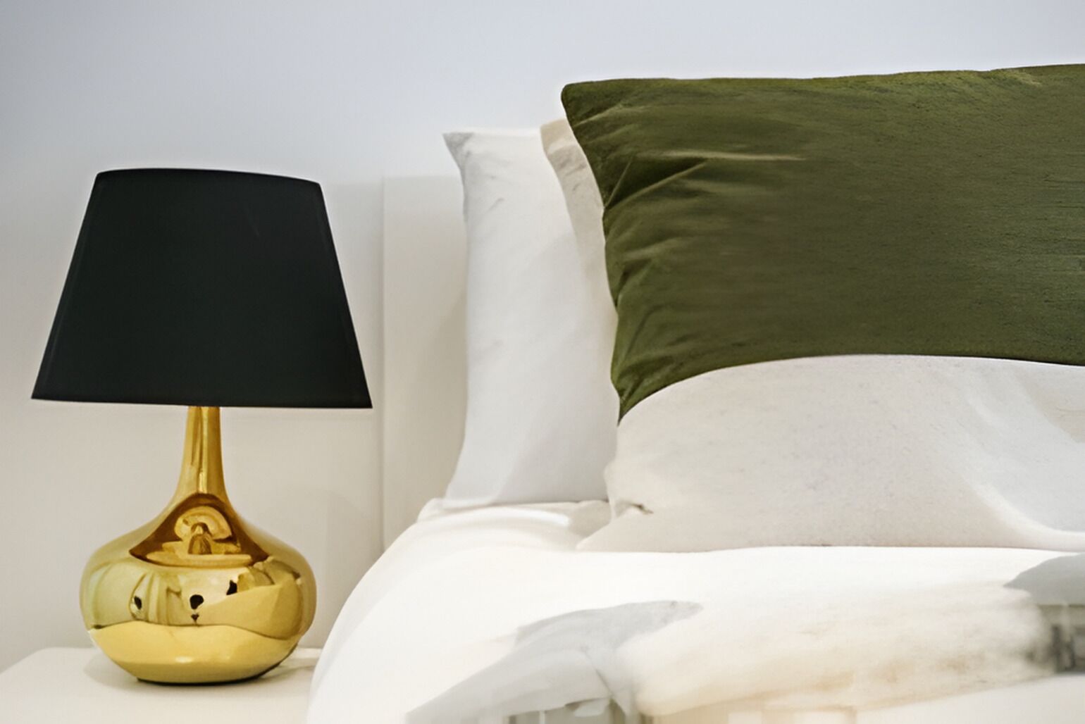 A bed with white and green pillows, a black lampshade, and a gold base.