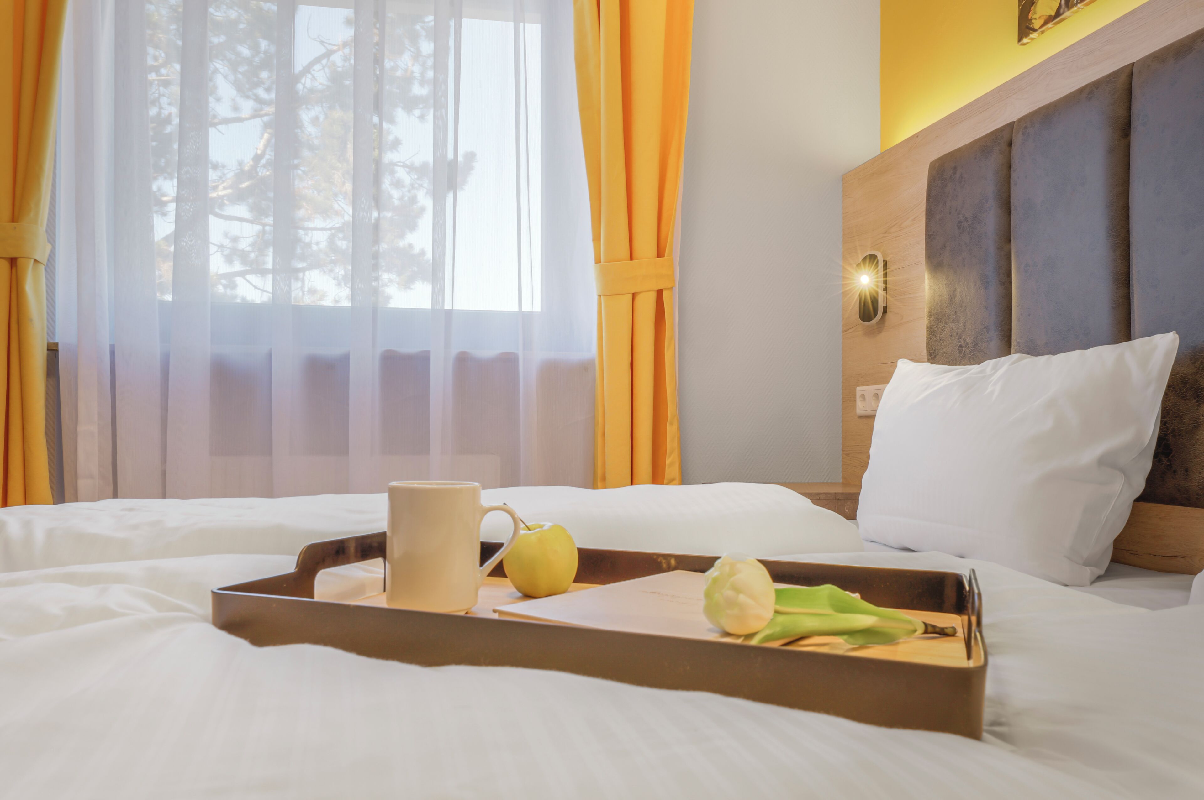 Une chambre d’hôtel avec un lit, un plateau sur lequel se trouvent une tasse, une pomme et une feuille verte.