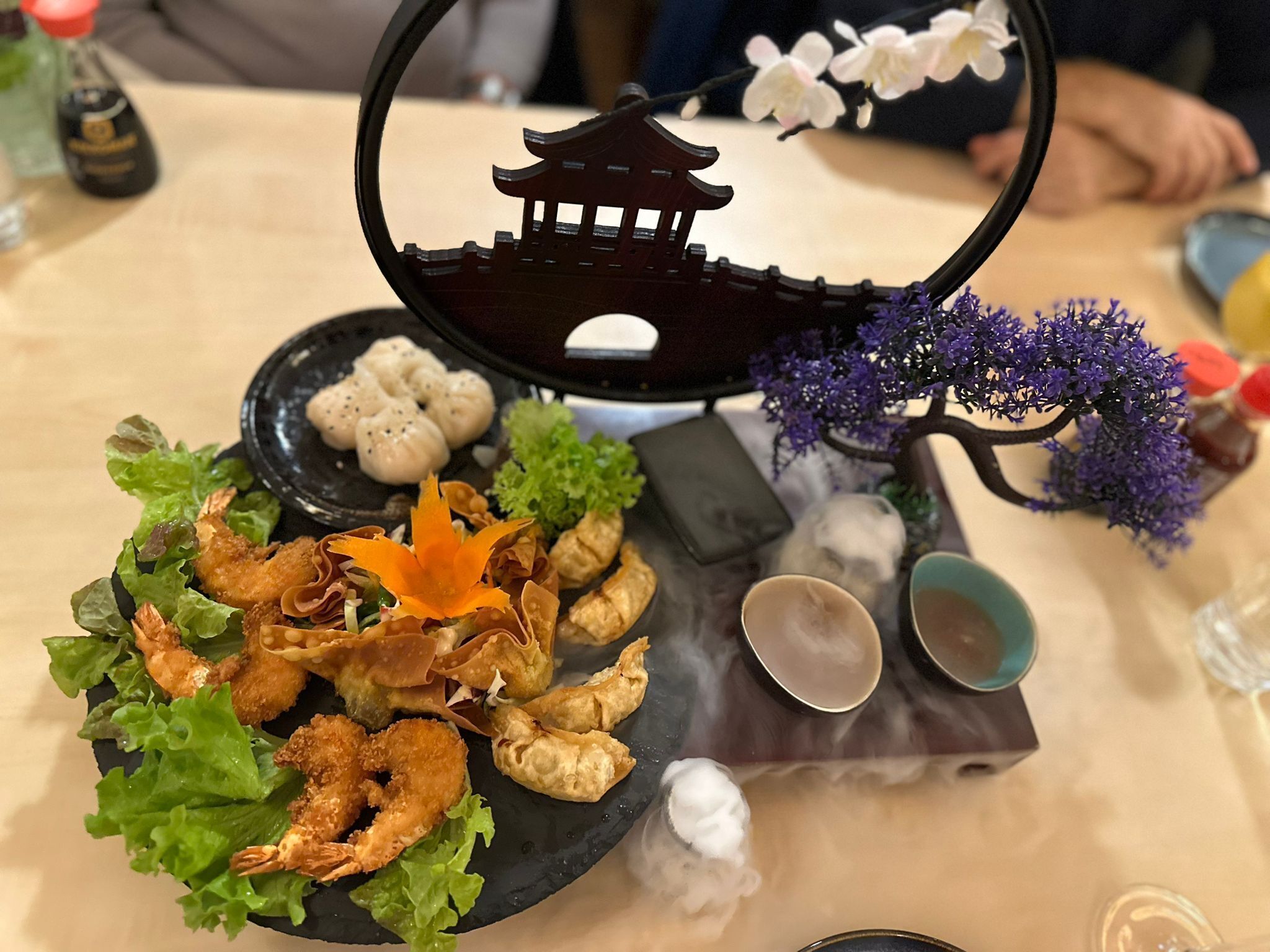 A table with a variety of food items, including fried shrimp, dumplings, and a decorative bonsai tree.