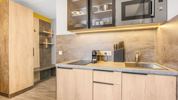 A modern kitchen with wooden cabinets, a built-in microwave, and a coffee maker. - XZLLENZ Hotel (Oberasbach)