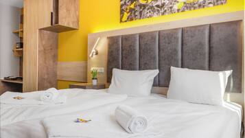Habitación de hotel con una cama grande, un armario de madera, una mesita de noche con lámpara y una pared amarilla decorada con un cuadro floral.