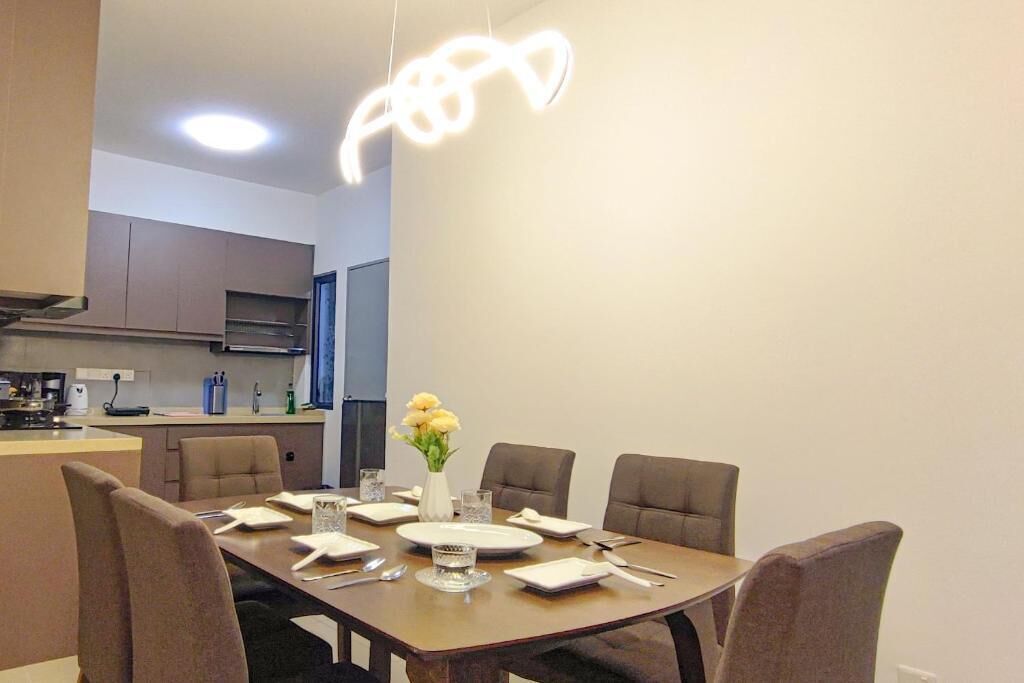 Een eetgedeelte met een tafel voor vier personen, een vaas met gele bloemen en een moderne hanglamp.