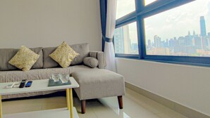 A modern living room with a sectional sofa, a coffee table, and a view of a city skyline through large windows. - Massive KL View at M-Vertica by HCK (Kuala Lumpur)