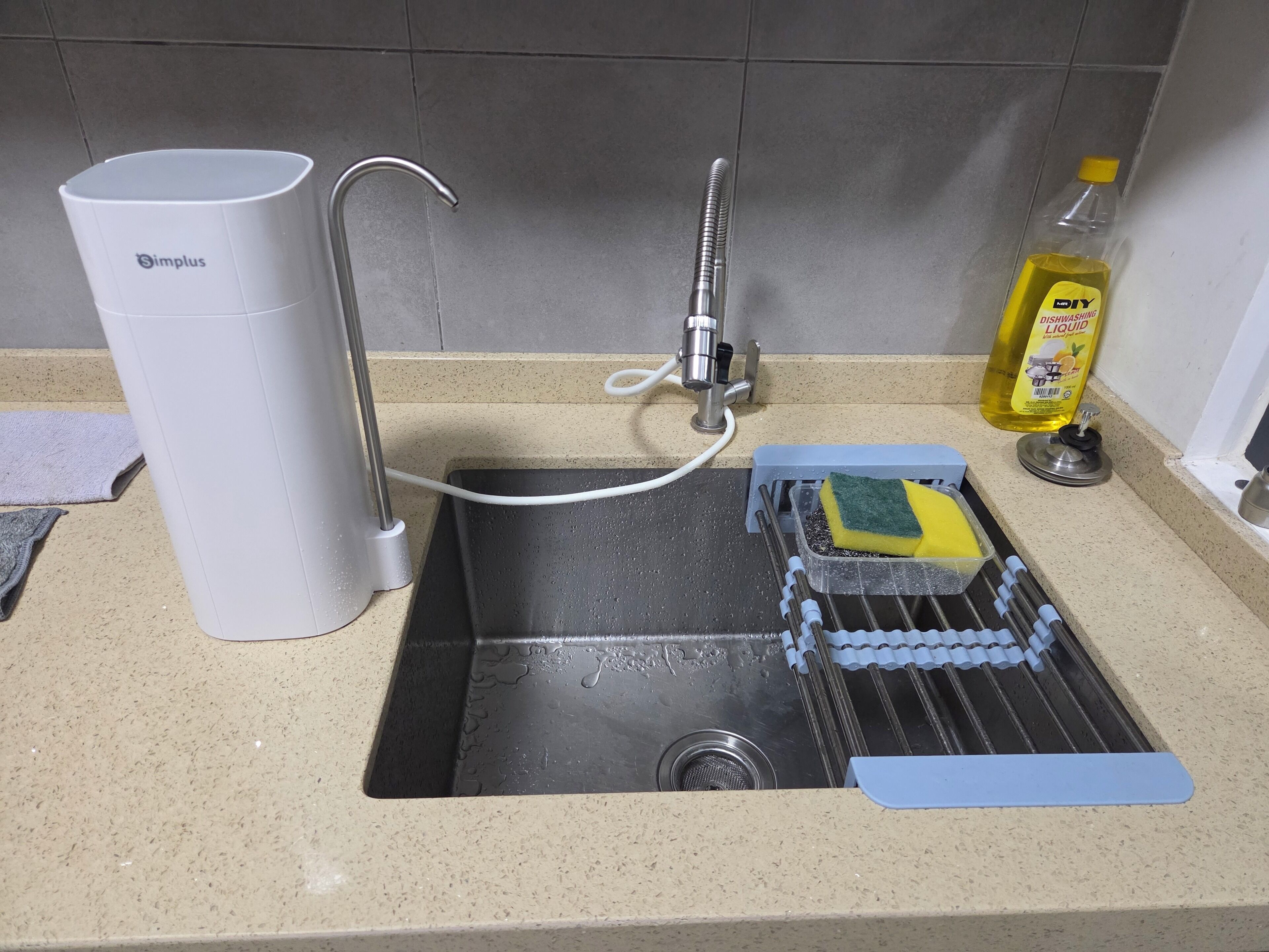 A kitchen sink with a faucet, a white Simplus water filter, a yellow bottle of dishwashing liquid, and a blue cleaning tool.