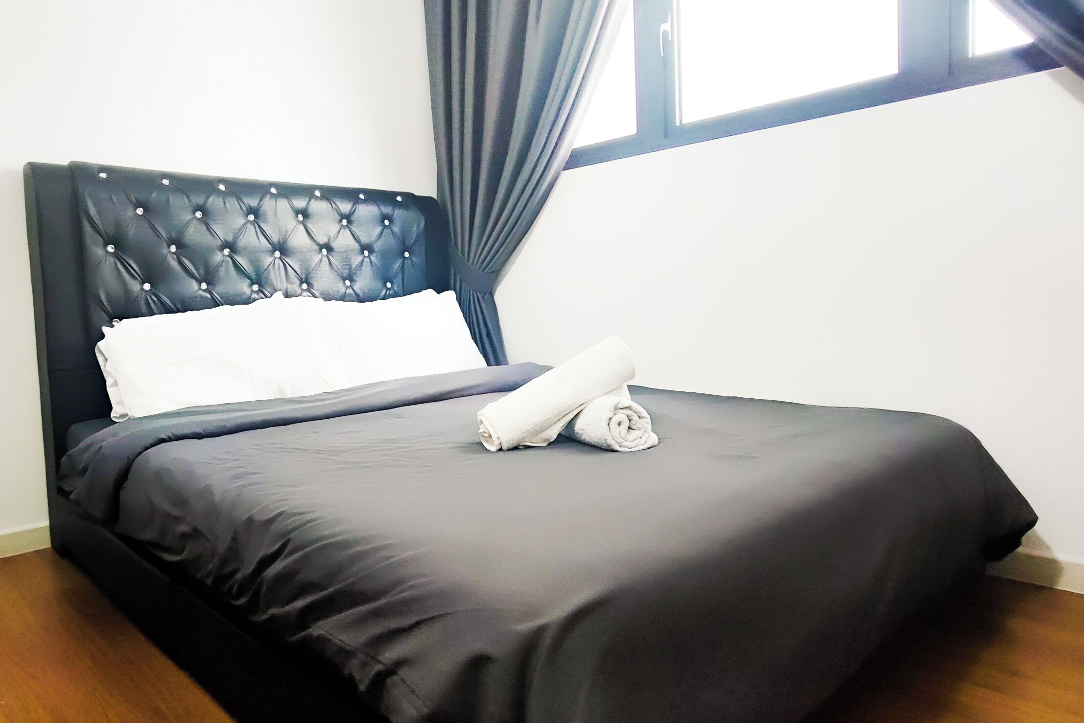 Ein ordentlich gemachtes Bett mit schwarzem Kopfteil, einem weißen Kissen und zwei aufgerollten Handtüchern.
