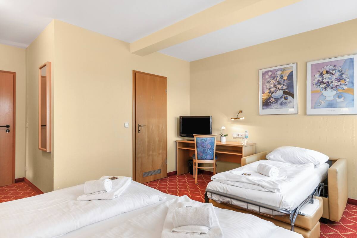 A hotel room with two beds, a desk with a chair, a television, and artwork on the wall.
