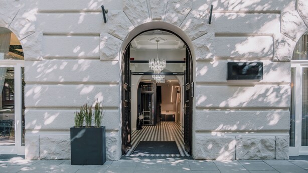 A grand entrance with a chandelier, a black mat, and a potted plant. - Dream Suites (Kraków)