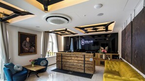 A modern hotel lobby with a reception desk, seating area, and a large painting on the wall. - Dream Suites (Kraków)