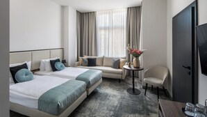 A hotel room with two beds, a sofa, a small table with a vase, a chair, and a TV. - Dream Suites (Kraków)