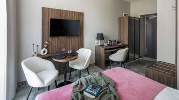 Et hotelværelse med en seng, to hvide stole, et skrivebord med tv, en lampe og et minibar.