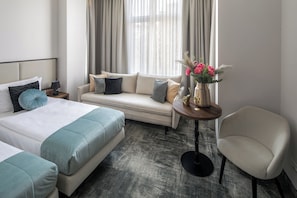 A hotel room with a bed, a sofa, a chair, a small table with a vase of flowers, and a window with curtains. - Dream Suites (Kraków)