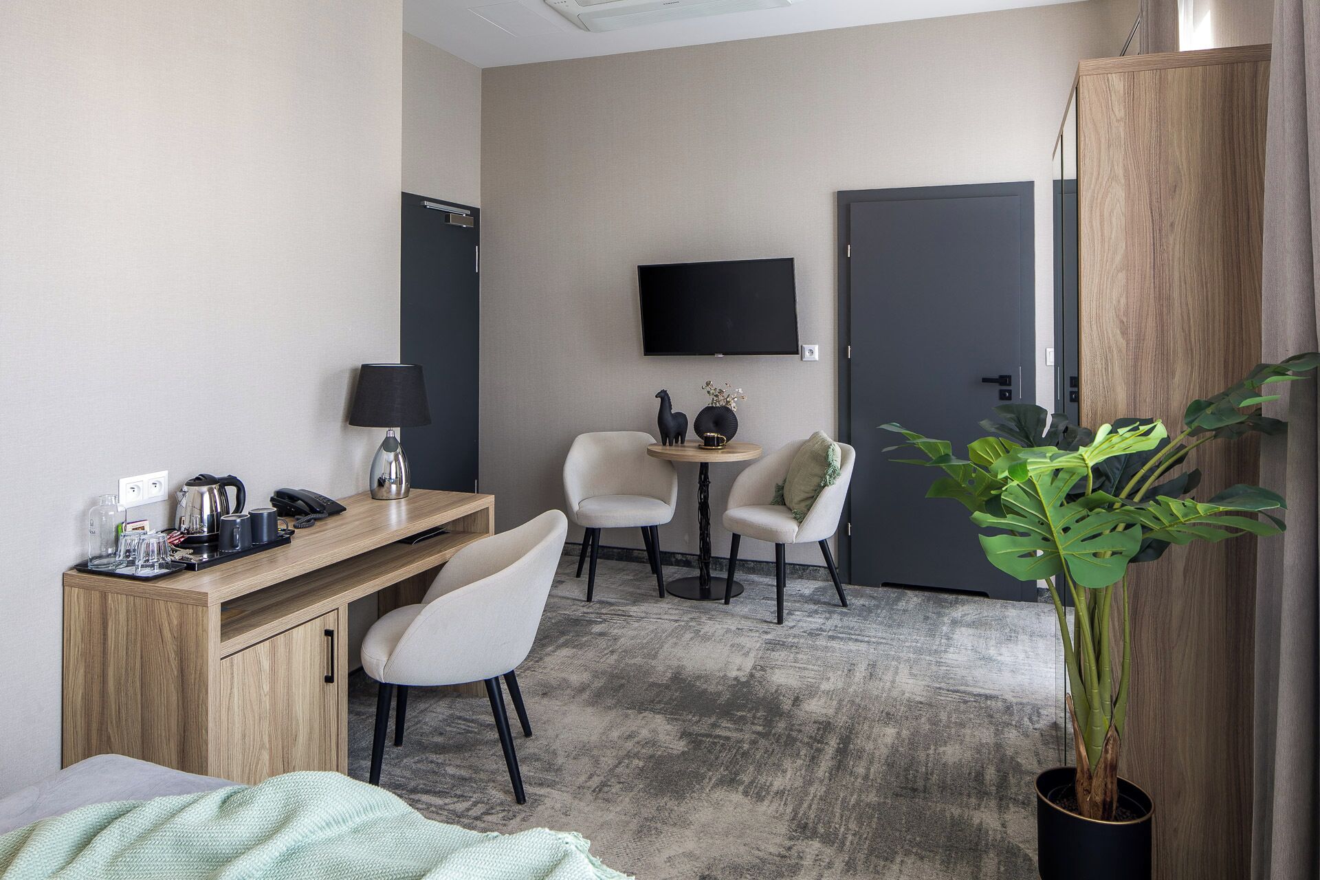 Ein Hotelzimmer mit Schreibtisch, zwei Stühlen, einem Fernseher, einer Tür und einer Zimmerpflanze.