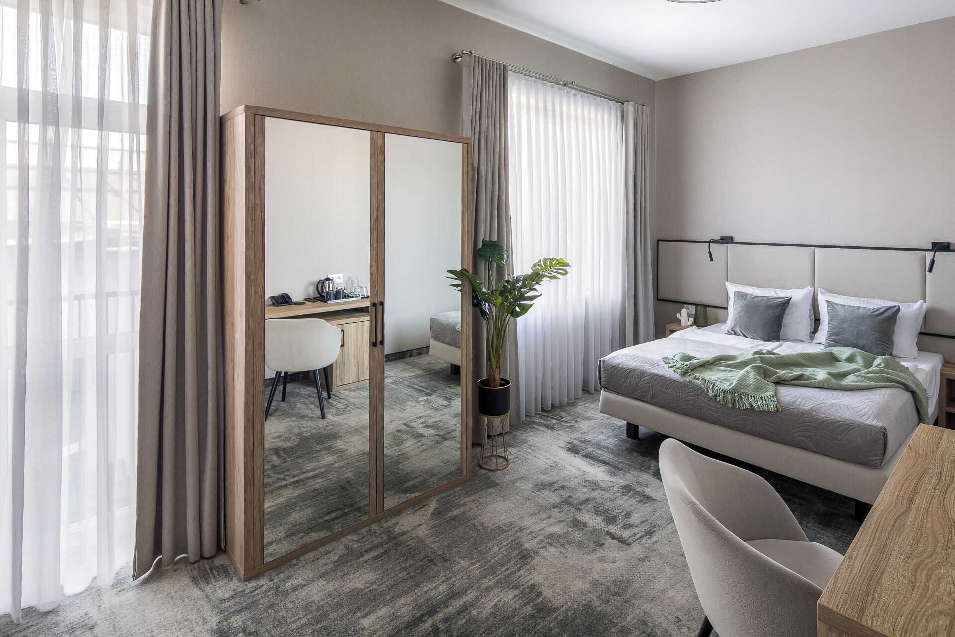 Habitación de hotel con cama, escritorio, silla, espejo y planta en maceta.