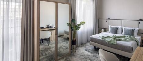 Habitación de hotel con cama, escritorio, silla, espejo y planta en maceta.