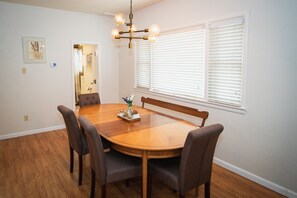 Un comedor con una mesa redonda de madera, seis sillas, una araña y una ventana con persianas.
