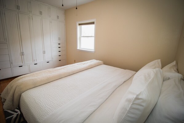 A bedroom with a bed, white bedding, a window, and a wardrobe.