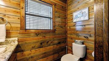 Un baño con paneles de madera, un inodoro, una ventana con persianas y un cuadro en la pared.