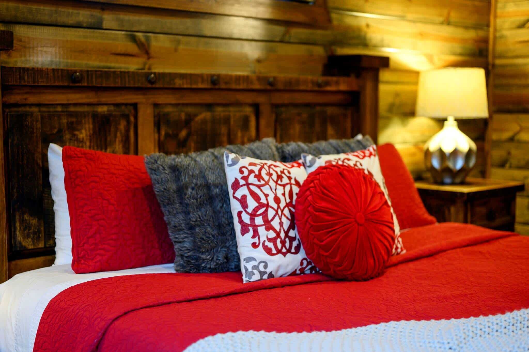 Un letto con cuscini rossi e grigi, una coperta rossa e una testiera in legno.