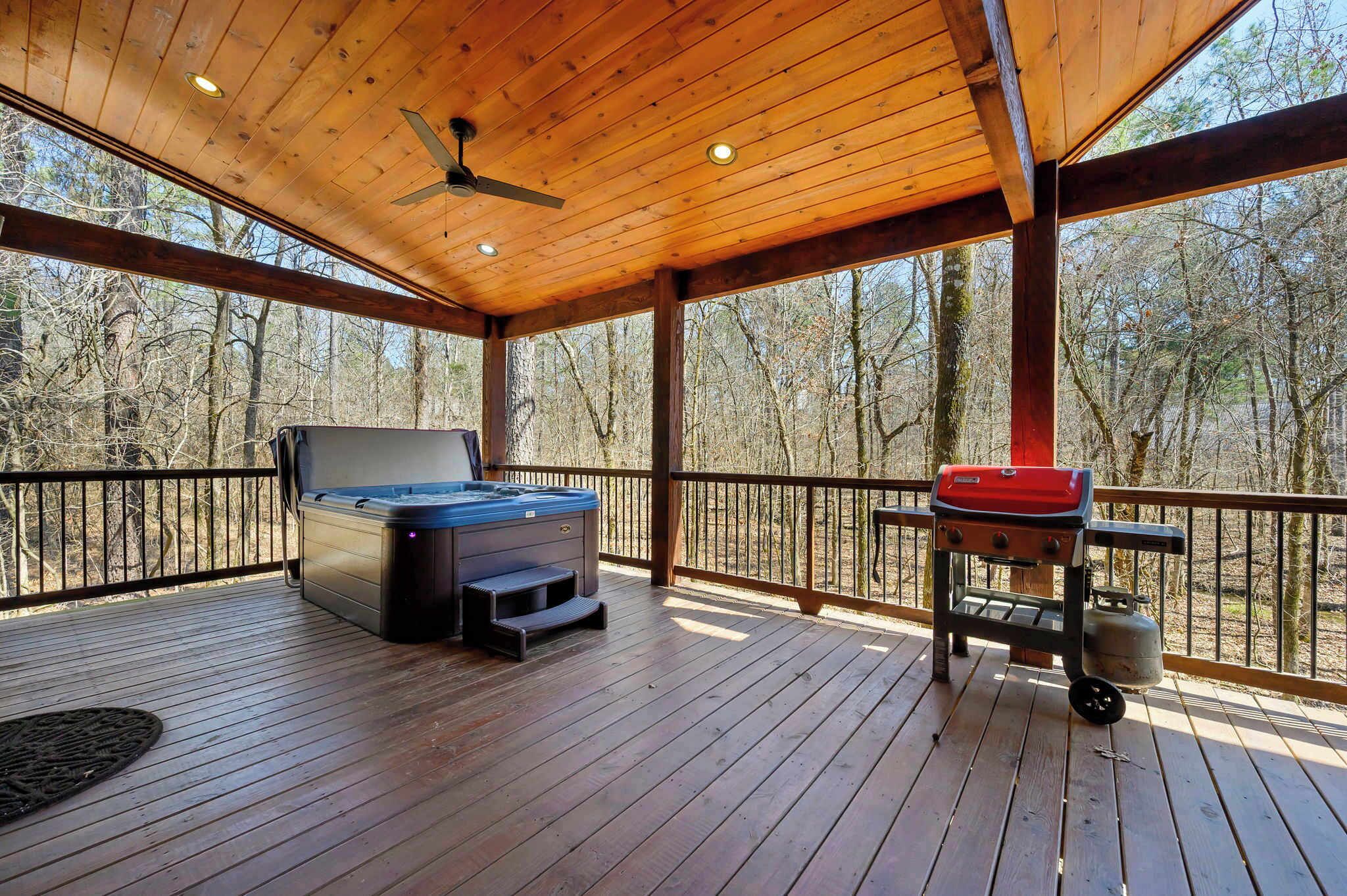 Eine überdachte Terrasse mit Whirlpool, Grill und Holzboden.