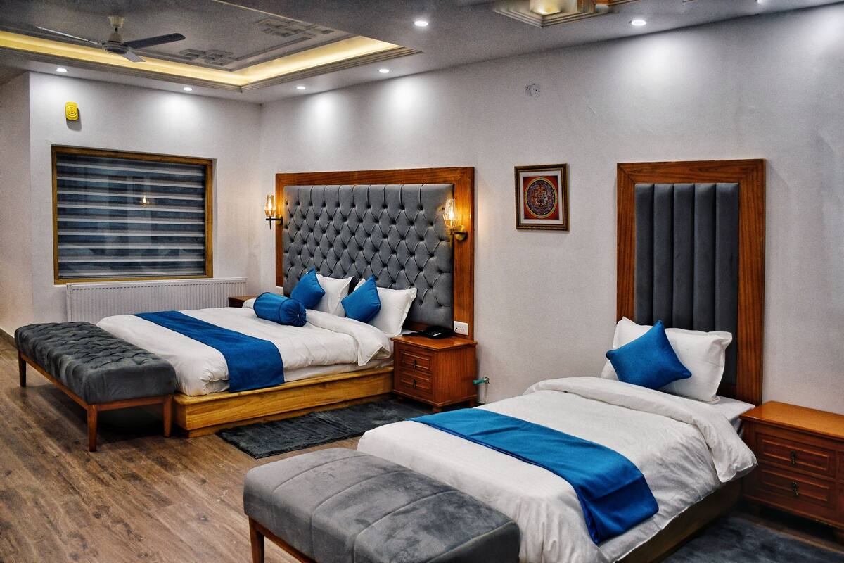 A hotel room with two beds, a large window with blinds, a ceiling fan, and a wooden headboard.
