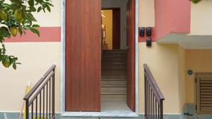 Un escalier menant à un espace intérieur, avec une porte en bois et une rampe en métal.