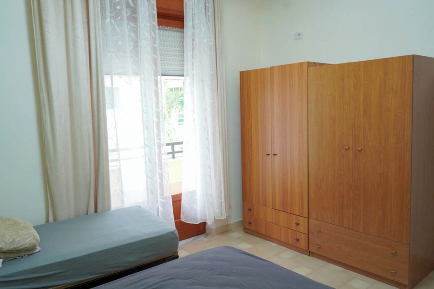 Une chambre à coucher avec un lit, une armoire et une fenêtre ornée de rideaux légers.