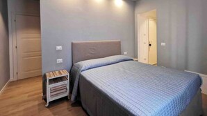 Un dormitorio con cama, mesita de noche, estante en la pared y una puerta.