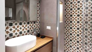 Un baño moderno con un espejo grande, un lavabo blanco, armarios de madera y baldosas con diseño.
