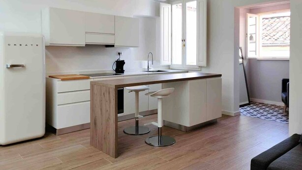 Una cocina moderna con armarios blancos, una isla de madera con taburetes de bar, horno empotrado y una lámpara colgante.