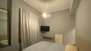 Un dormitorio con cama, televisor montado en la pared, radiador y ventana con cortinas.
