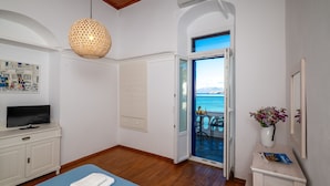 Een slaapkamer met een bed, een televisie op een dressoir, een deur naar een balkon en uitzicht op zee.