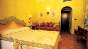 Une chambre d’hôtel avec un grand lit, une table de chevet sur laquelle se trouve un panier de fruits, une commode et un téléviseur.