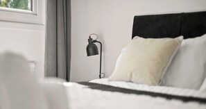 Une chambre à coucher avec un lit, une table de chevet, une lampe et une fenêtre.