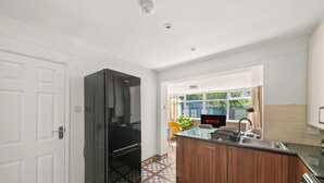 Une cuisine moderne avec un réfrigérateur noir, des armoires en bois, un évier et un coin repas agrémenté d’une chaise jaune.
