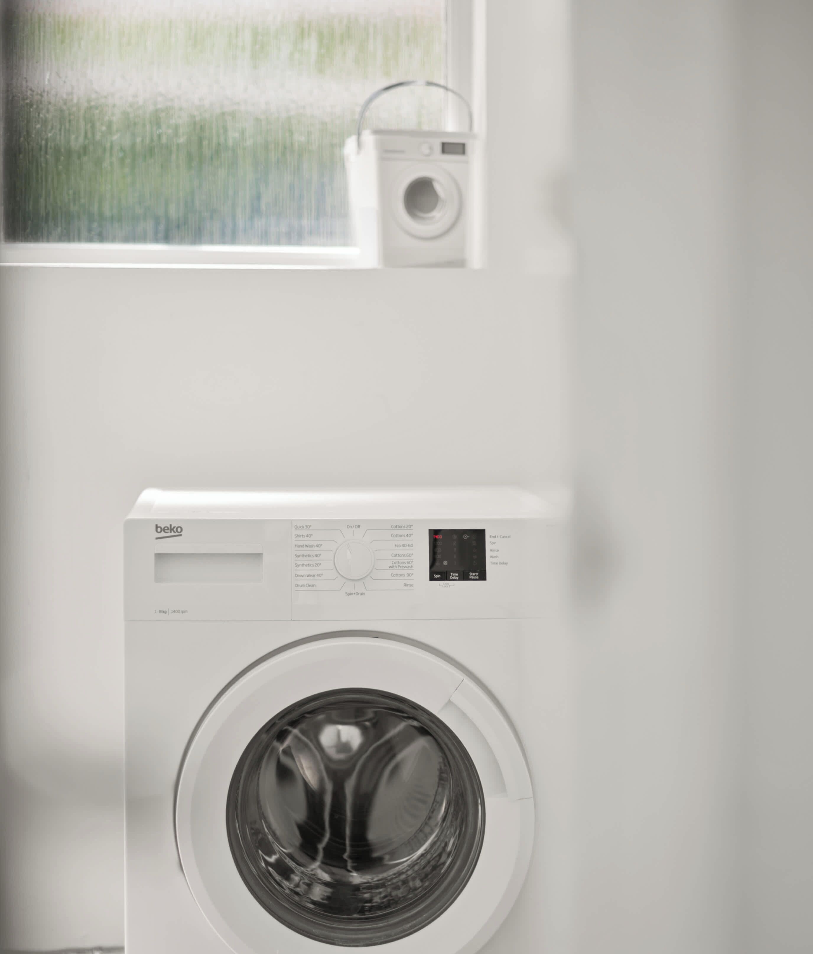 A front-loading washing machine with a control panel, a small window above it, and a door.