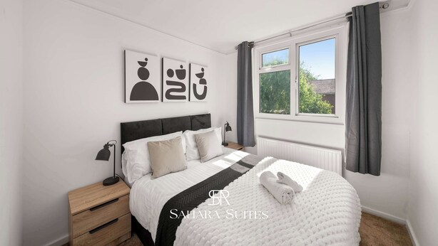 Une chambre à coucher avec un lit, des tables de chevet, une fenêtre avec des rideaux et des œuvres d’art murales.